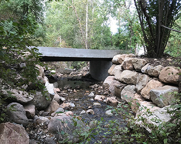 Rock walls on each side of a creek that leads under a bridge