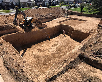 Excavator digging a large basement with worker standing at bottom