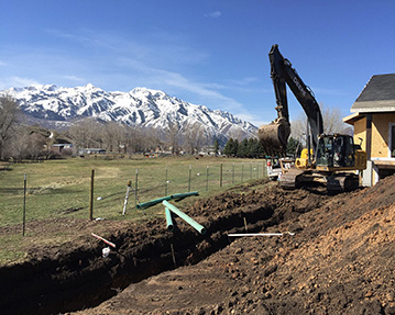 Excavator digging a trench for utilities with snowy mountains in background