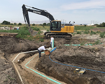 Excavator and worker backfill pipe that is in trench