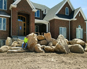 Worker rests against a large rock while sitting on rock stairs in front of house