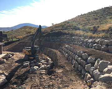 Three levels of a large rock wall with excavator moving rocks